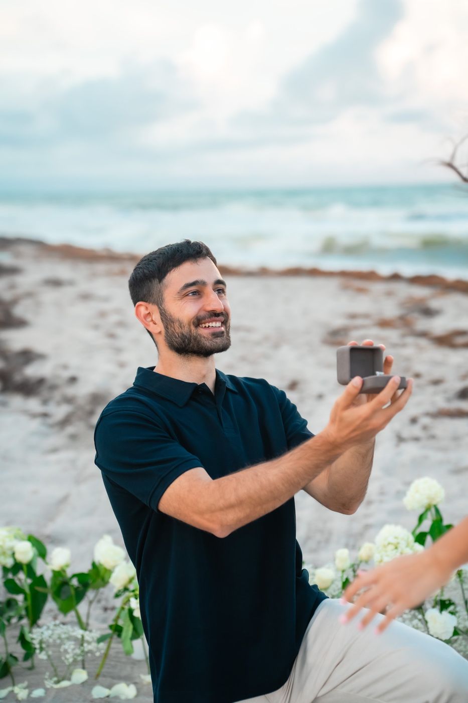 Sahar on one knee holding an open ring box, smiling